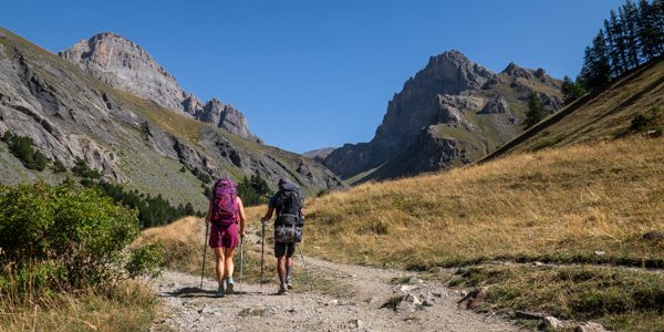 Deux personnes portant des sacs a dos en randonnée itinérante, avec vue sur des montagnes des Alpes