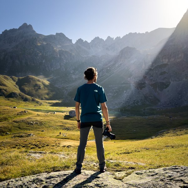 Homme seul de dos tenant un appareil photo dans sa main face a un paysage de montagne